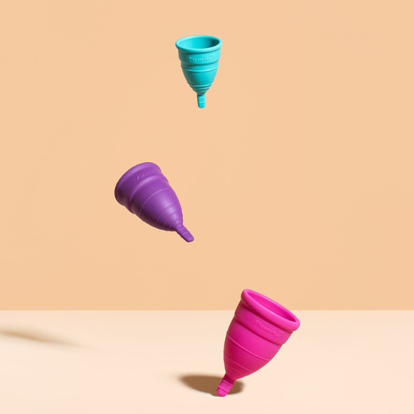 Coletores menstruais coloridos flutuando sobre fundo pêssego