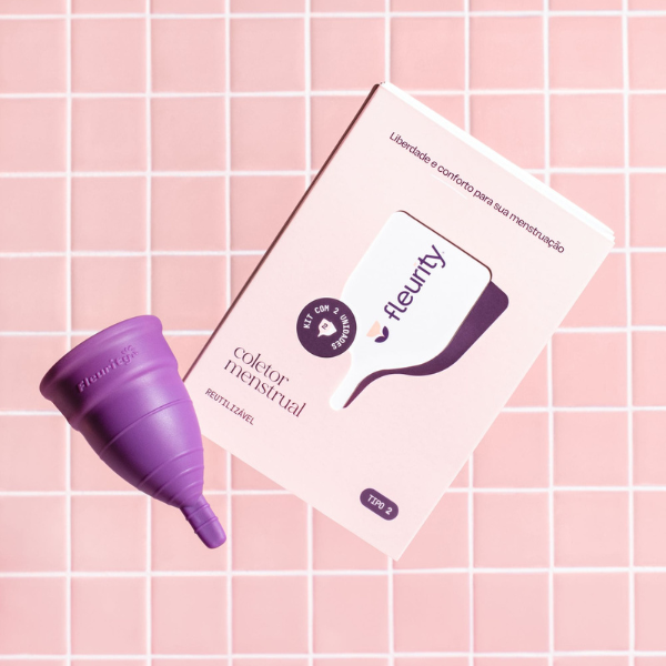 Coletor menstrual roxo e a caixa Fleurity sobre azulejos rosa