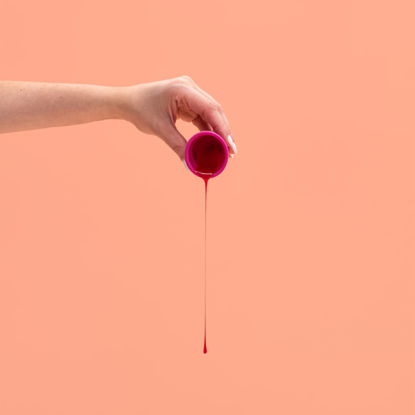 Mão segurando um coletor menstrual sobre fundo coral
